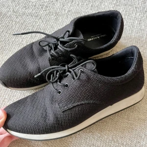 Svarta sneakers från Vagabond - Svarta sneakers från Vagabond med stickad ovandel och rund tå. Skorna har snörning och en vit platt sula som ger en clean look. Perfekta för dig som gillar enkel och stilren design med sportig känsla.