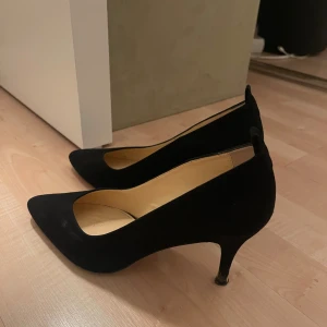 Svarta klackar från Decadent Copenhagen - Stilrena svarta klackar från Decadent Copenhagen (äkta) i mocka med spetsig tå och smal klack. Klassisk och elegant design som lyfter vilken outfit som helst. Skorna har en mjuk innersula i skinn och en snygg siluett som passar perfekt till dig som gillar en tidlös look. Under sidan ser mer sliten ut än de är då de mesta är smuts. Pris kan diskuteras vid snabb affär.