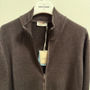 Gran Sasso zip - Snygg brun kofta från Gran Sasso med hel dragkedja och ribbad krage. Tillverkad i mjuk ull som känns skön mot huden. Perfekt att slänga på sig när det är lite kyligt ute. Stilren design med långa ärmar och diskreta detaljer. Storlek 52 passar M