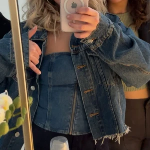 Jeans tubtopp med dragkedja - Säljer en snygg jeans tubtopp i klassisk blå denim med markerade sömmar och en dragkedja framtill. Toppen är axelbandslös och har en figurnära passform. Perfekt till fest. Toppen är använd men i bra skick.