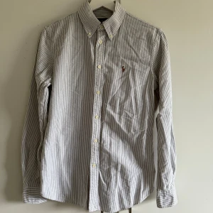 Randig skjorta från Ralph Lauren - Klassisk skjorta från Ralph Lauren i vitt och grått med smala vertikala ränder. Skjortan har lång ärm, knappar framtill och broderad logga på bröstet. Custom fit-modell i mjuk bomull, perfekt för en clean och stilren look. Liten i storleken så sitter som xs typ