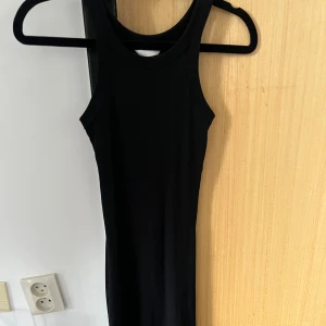 Svart ärmlös ribbad klänning - En svart, tight och ärmlös klänning med ribbad struktur. Klänningen har en sportig, hög ringning och är figurnära i modellen. Perfekt för dig som gillar en enkel och stilren look.