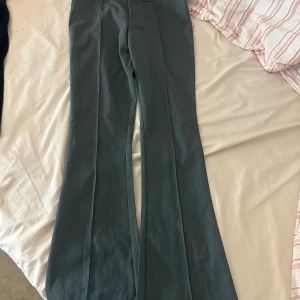 Grå kostymbyxor med bootcut - Snygga grå kostymbyxor från H&M med bootcut-silhuett och pressveck längs benen. Byxorna har hög midja och stängs med dold dragkedja fram. Perfekta för en clean och stilren look.