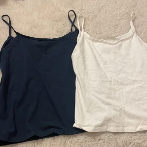 Marinblå och vit linnetopp Gina Tricot - Två stilrena linnetoppar från Gina Tricot, en i marinblått och en i vitt. Dom kommer i ett pack. Båda har smala axelband och rak, enkel passform. Perfekta att matcha med jeans eller shorts. Materialet är mjuk bomull som känns skönt mot huden. Linnena är lite luftigare och sitter inte så tajt och är lite kortare i längden, som en magtröja. Jag har knappast använt dom.