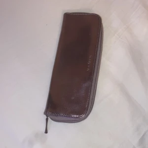 Lila sminkborts nässeser från Mary Kay - Slimmad lila sminkborts nessäser från Mary Kay i glansigt syntetmaterial. Stängs med dragkedja och har flera fack på insidan för sminkborstar eller pennor. Perfekt att ha i väskan för att hålla ordning på småsaker.