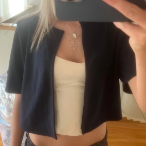 Mörkblå croppad overshirt - Snygg mörkblå croppad overshirt med korta ärmar och rak passform. Jackan har en enkel, stilren design utan knappar eller dragkedja och är tillverkad i ett mjukt material som känns skönt mot huden. Perfekt att slänga över en topp för en chill look.