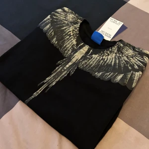 Marcelo Burlon svart tröja med vingar - Svart långärmad tröja från Marcelo Burlon County of Milan med ikoniskt vingtryck i grått över axlar och bröst. Tröjan har rund halsringning och är tillverkad i mjuk bomull. Perfekt för dig som vill sticka ut med en unik design.