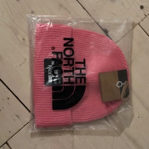 Rosa mössa från The North Face - Helt ny Rosa ribbstickad mössa från The North Face med klassisk uppvikt kant och den klassiska logga framtill. Perfekt accessoar för kyliga dagar och en snygg detalj till din outfit. Levereras i orginalfärpackning. 