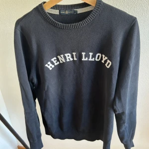 Mörkblå tröja från Henri Lloyd - Snygg mörkblå tröja från Henri Lloyd med vit logotyp framtill. Klassisk rund halsringning och ribbade muddar vid ärmslut och nederkant. Perfekt för dig som gillar stilrena och tidlösa plagg.