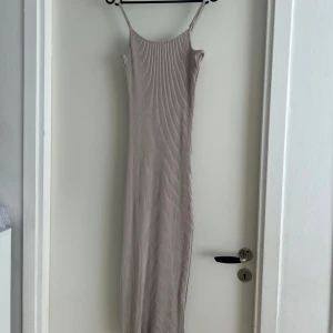 Beige ribbad långklänning - Säljer en beige ribbad långklänning med smala axelband och figurnära passform. Klänningen har en enkel och stilren design med vertikala ribbor som ger en snygg struktur. Perfekt för dig som gillar minimalistisk stil.