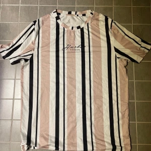 Randig t-shirt - Snygg t-shirt Harban med breda vertikala ränder i svart, vitt och beige. Klassisk rund halsringning och korta ärmar. Skön och lätt i bomullsmaterial, perfekt för en chill och stilren look.