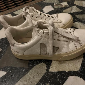 Vita Veja sneakers, stl 36 - Snygga vita Veja sneakers med beige detaljer och klassisk V-logga på sidan. Modellen har rund tå, platt sula och snörning. Perfekta för dig som gillar stilrena och minimalistiska sneakers med en clean vibe.