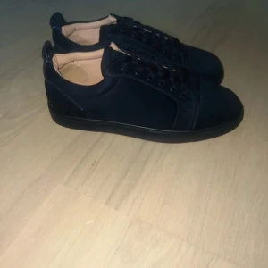 Mörk blåa sneakers från Christian Louboutin - Snygga svarta sneakers från Christian Louboutin i mocka med klassisk röd sula och diskret broderad logga på hälen. Skorna har rund tå, svarta snören och en stilren design som passar perfekt till streetwear eller en mer dressad look. Säljer lite billigare pga box.skriv vid minsta undringen mvh Gustav.