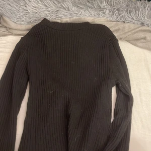 Svart ribbad tröja från FASISTER - Svart långärmad tröja från FASISTER i storlek XXS. Tröjan är ribbad och har en högre rund halsringning. Perfekt basplagg med tight passform som funkar till allt. Materialet känns mjukt och stretchigt.