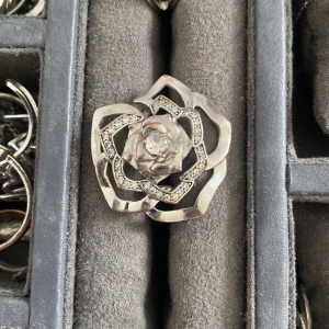 Stor silverfärgad blomring med stenar - Statementring i silverfärg formad som en stor blomma med glittrande stenar i kronbladen och en gnistrande sten i mitten. Ringen har en öppen, detaljerad design som verkligen sticker ut och ger en cool vibe till din look. Den är från ioaku och är lite rostig.