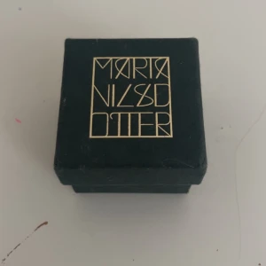 Silverhalsband Marta Nilsdotter - Unikt silverhalsband från Marta Nilsdotter med en cool, kantig berlock i form av ett ansikte. Kedjan är grov och har en modern vibe, perfekt för dig som gillar statement-smycken. Märkt med Dotter 925 på baksidan av berlocken. Levereras i original ask.