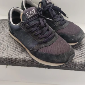 Svarta sneakers från EA7 Emporio Armani - Snygga svarta sneakers från EA7 Emporio Armani med klassisk design. Skorna har ovandel i mesh och mocka, vita detaljer på sulan och logga på plös och häl. Perfekta för dig som vill ha en stilren och sportig look.
