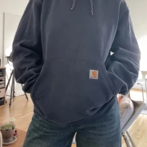 Mörkblå Carhartt hoodie med huva - Säljer en mörkblå hoodie från Carhartt i storlek M. Tröjan har huva med dragsko, stor magficka och klassisk Carhartt-logga framtill. Tillverkad i 80% bomull och 20% polyester för en skön och avslappnad känsla. Så fin, skriv för frågor.