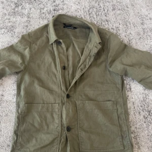 Olivgrön overshirt från J.Lindeberg - Snygg olivgrön overshirt från J.Lindeberg med klassisk krage, stora framfickor och knäppning framtill. Tillverkad i bomull med lite elastan för extra komfort. Perfekt lager-på-lager-plagg med avslappnad vibe. Mitt pris 550kr nypris ca 2500kr. Priset går självklart att diskutera.