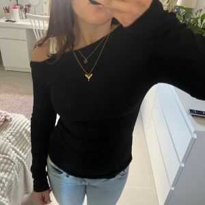 Svart offshoulder långärmad topp - Säljer en svart långärmad topp med offshoulder-design. Snygg och enkel modell som sitter tight och har en stilren look. Perfekt att matcha med jeans eller kjol för en trendig outfit.