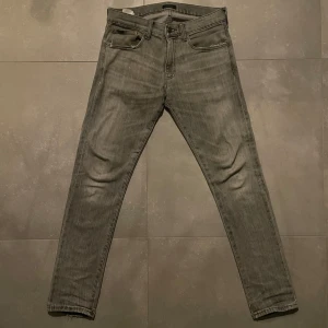 Ralph Lauren jeans - Slim fit jeans från Polo Ralph Lauren i modellen Sullivan Slim. Jeansen är grå med snygg tvätt och klassiska fem fickor. Tillverkade i mjukt denimtyg med diskreta slitningar och raka ben. Perfekta för en clean och stilren look. Storlek 30/32