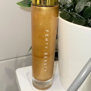 Fenty Beauty Body Lava Trophy Wife - Body Lava från Fenty Beauty i nyansen Trophy Wife, en flytande highlighter med intensivt guldskimmer. Kommer i en lyxig glasflaska med guldfärgat lock och pump. Perfekt för att ge kroppen en glittrande glow och highlight-effekt.