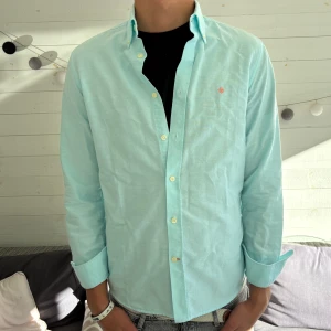 Ljusblå skjorta från Morris - Snygg ljusblå skjorta från Morris med klassisk krage och knappar framtill. Skjortan har lång ärm och en liten broderad logga på bröstet. Perfekt för dig som gillar stilrena och fräscha plagg. Tillverkad i mjuk bomull för skön känsla.