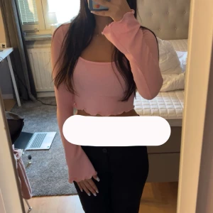 Rosa croppad topp från SHEIN - Säljer en ljusrosa croppad topp från SHEIN i ribbat material. Toppen har långa ärmar, fyrkantig ringning och vågig volangkant nertill. Perfekt för dig som gillar en söt och trendig stil.