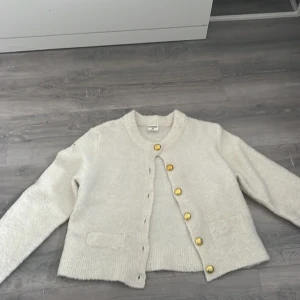 Vit kofta  med guldknappar - Mysig vit kofta från H&M med snygga guldknappar framtill. Koftan är stickad och har två små fickor framtill samt rund halsringning. Perfekt för lager-på-lager och passar till allt. Långärmad och i mjukt material.
