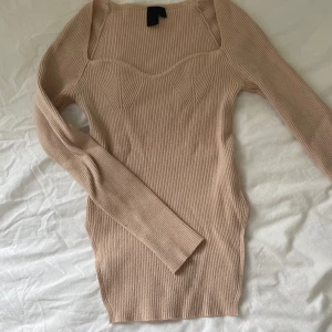 Beige ribbad stickad kortklänning - Supersnygg beige ribbad stickad klänning med lång ärm och markerad byst. Tight passform och fyrkantig ringning ger en modern vibe. Perfekt för dig som gillar stilrena och trendiga plagg.