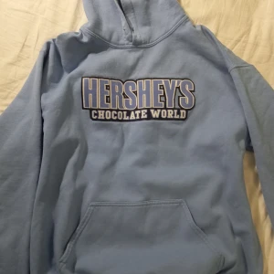 Ljusblå Hershey's hoodie - Säljer en ljusblå hoodie från Hershey's Chocolate World. Den är fin men är använd, ändå tydliga tecknet är de lilla färgtrycket på ena ärmen (se bild tre?