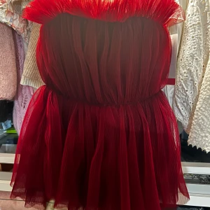 Röd volangklänning/topp från H&M Edition - Supersnygg röd kortklänning/topp från H&M Edition med volangdetaljer och plisserad tyll. Axelbandslös modell som ger en riktigt statement-look. Perfekt för dig som vill sticka ut med en dramatisk och trendig stil.