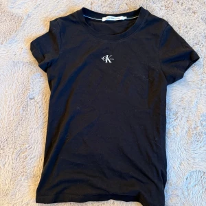 Svart t-shirt från Calvin Klein Jeans - Svart t-shirt från Calvin Klein Jeans med klassisk passform och liten CK-logga broderad på bröstet. T-shirten är kortärmad och tillverkad i mjuk bomull, perfekt för en clean och stilren look.