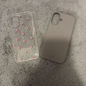 Holdit mobilskal och hjärtmönstrat skal - Två mobilskal i fint skick: ett transparent skal med rosa hjärtan och ett enfärgat grått Holdit-skal. För iPhone 16. 