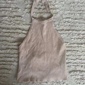 Beige stickad halterneck linnetopp - Säljer en beige stickad halterneck topp med knyt i nacken. Toppen är ärmlös och har en croppad passform som ger en trendig look. Gått upp lite i sömnen, se bild