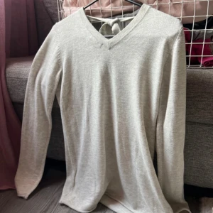 Grå långärmad tröja med knyt i ryggen - Supermjuk grå långärmad tröja från H&M med v-ringning framtill och snygg knytning i ryggen. Tillverkad i tunn stickad bomullsblandning, perfekt för lager-på-lager. Enkel och stilren design som funkar året runt.