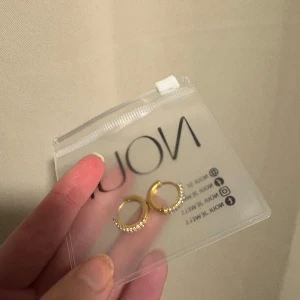 Örhängen  - Snygga små hoops från Noui i guldton med glittrande stenar på framsidan. De är runda och har en klassisk men trendig look som passar perfekt till att lyfta vilken outfit som helst. Kommer i originalask. Helt nya, vattentåliga och allergifri!