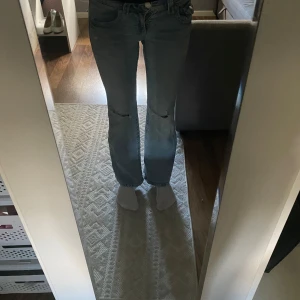 Ljusblå jeans från Gina Tricot - Säljer ett par ljusblå lowwaist bootcut jeans från Gina Tricot med slitningar vid knäna. Jeansen har klassiska fickor både fram och bak, samt knappdetalj på bakfickorna. Perfekta för en avslappnad och trendig look.