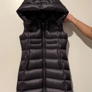 Mörk grå lång dunväst från Monel - Lång, mörk grå dunväst från Monel med huva. Västen har dragkedja framtill och även på baksidan. Köpt på johnells för 4999kr. Använd 1 gång. Superfin och unik kommer bara tyvärr inte till användning. Perfekt nu till hösten. Pris går att diskutera💓