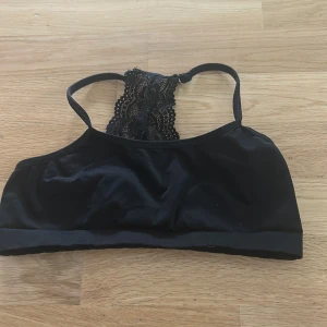 Svart spetsdetaljerad linnetopp - Svart linnetopp med tunna axelband och snygg spetsdetalj i ryggen. Tillverkad i stretchigt material med 90% polyamid och 10% elastan. Perfekt för en trendig och bekväm look, funkar lika bra till jeans som kjol.