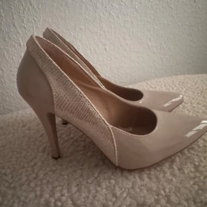 Snygga pumps - Använd bara en gång, storlek 36, innelängd 23cm, klack 9cm. Färg beige med guldiga detaljer på sidorna.