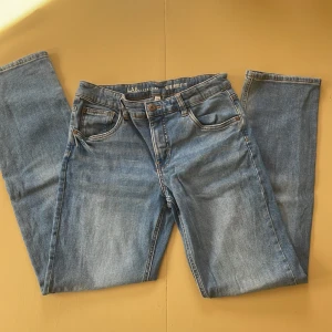 Blå retro jeans från LAB Industries - Snygga blå jeans från LAB Industries med retro-vibe och regular fit. Klassisk femficksmodell, raka ben och ljus tvätt med subtila slitningar. Jeansen har knappstängning och tydliga kontrastsömmar. Perfekt för dig som gillar en avslappnad och tidlös stil.