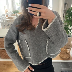 Grå stickad kofta från Zara - Superfin grå stickad kofta från Zara med kontrastfärgade vita kanter och två stora fickor framtill. Koftan är croppad med v-ringning och har en loose fit som ger en chill vibe. Perfekt att slänga på sig över ett linne eller t-shirt. Jätte trendig och slutsåld. Storlek L men passar min som vanligtvis har S-M