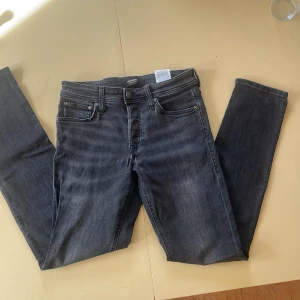 Jack & Jones Slim Glenn jeans mörkgrå - Slim Glenn jeans från Jack & Jones i mörkgrå tvätt med snygga slitningar. Modellen har fem fickor, smal passform och klassisk knappstängning. Perfekt för dig som gillar en modern och stilren look. Materialet är mjukt och stretchigt jeans.