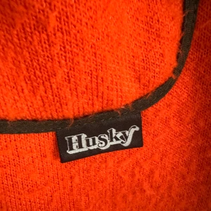 Röd fleecejacka från Husky - Riktigt snygg röd fleecejacka från Husky med svarta detaljer längs kanterna och dragkedja framtill. Jackan har en enkel bröstficka och en sportig vibe, perfekt för kyliga dagar. Skön och mjuk känsla, passar dig som gillar färg och stil.