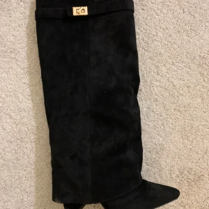 Svarta mockastövlar med spetsig tå - Snygga svarta stövlar i mocka med spetsig tå. Stövlarna har en stilren design med en liten gulddetalj upptill. Perfekta för dig som vill ha en klassisk och trendig look. Bara använda en gång!