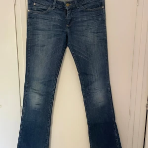Lowaist bootcut jeans från Wrangler - Snygga blå jeans från Wrangler med klassisk bootcut-modell och slitna detaljer. Dom är långa och passar mig perfekt, (jag är 180) Det har en liten söm bredvid den högra bakfickan (se bild 4), men det är inget som man lägger märke till. Skriv vid frågor, exakta mått eller fler bilder💕