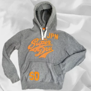 Superdry Hoodie - Snygg Superdry hoodie i storlek M – enkel att matcha och skön att bära. Ett stilrent val, noggrant utvalt med omsorg av AM Clothing.  📩 Frågor? Hör gärna av dig! 📲 Följ oss här på Plick för fler uppdateringar. ♻️ Tack för att du handlar mer hållbart med AM Clothing!