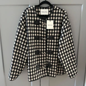 Rutig jacka från Malina i ullmix - Snygg rutig jacka från Malina i svart och vitt med coola spänndetaljer framtill. Jackan är aldrig använd då den inte passar på mig! Jag är en S och den sitter snyggt oversized!💕