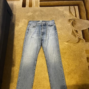 Ljusblå jeans från 157 Seattle W32 L34 - Säljer ett par ljusblå jeans från 157 Seattle i klassisk rak modell. Jeansen har fem fickor, knappgylf och slitna detaljer vid benslut och lår. Perfekt för dig som gillar en avslappnad och tidlös look.